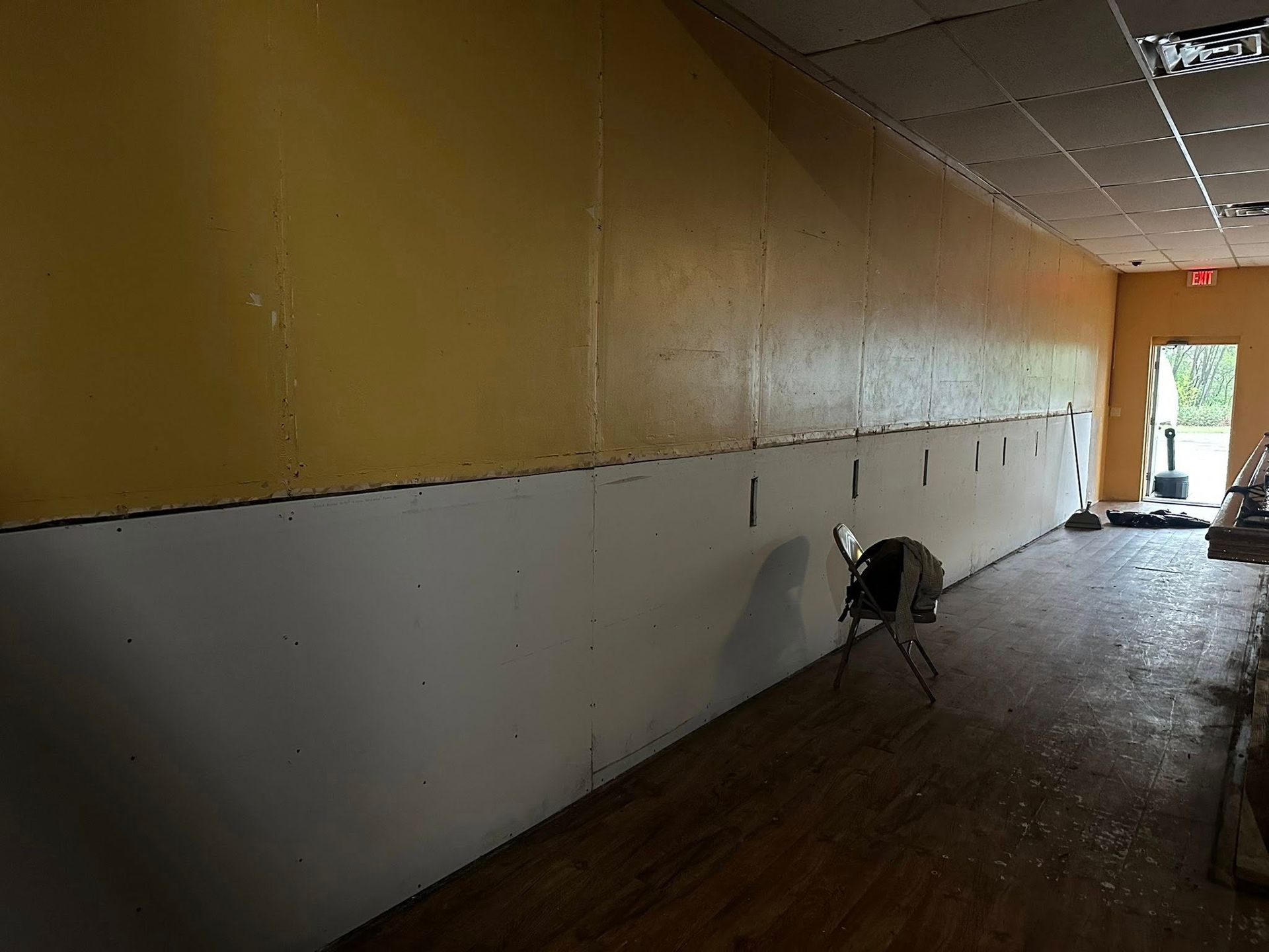 Interior of a room with exposed walls; yellow upper and white lower; a chair sits on a wood floor leading to an open doorway.