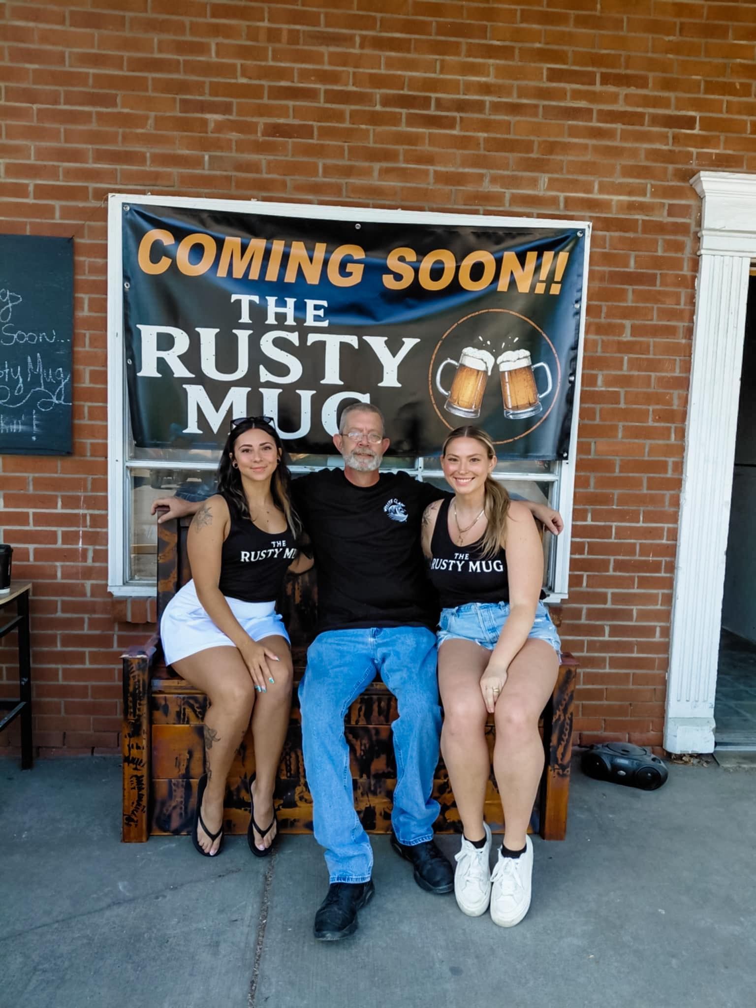 Three people posing in front of a banner for a bar, 