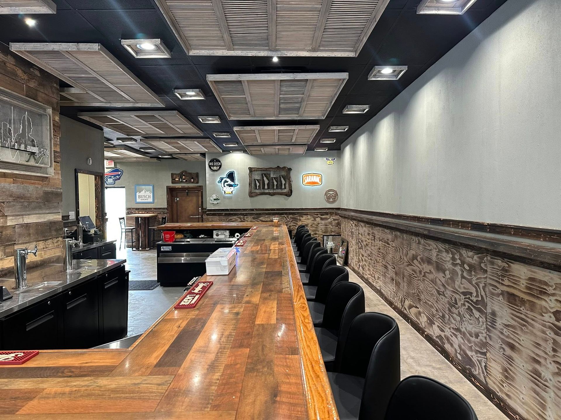 Interior of a bar with a wooden counter, black chairs, and rustic wall decor.