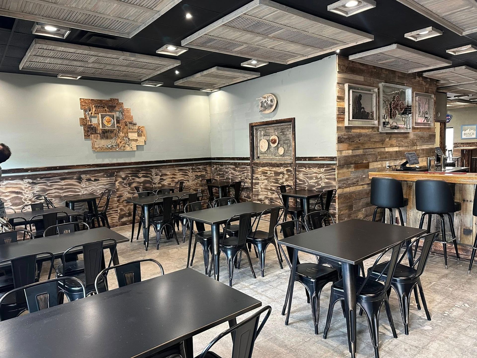 Interior of a restaurant with black tables and chairs, wood accents, and a textured ceiling.
