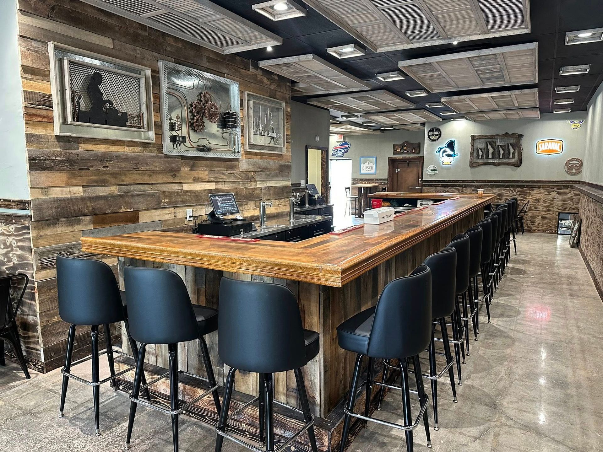 Bar interior with rustic wood paneling, long bar with stools, artwork on the wall, and decorative ceiling panels.