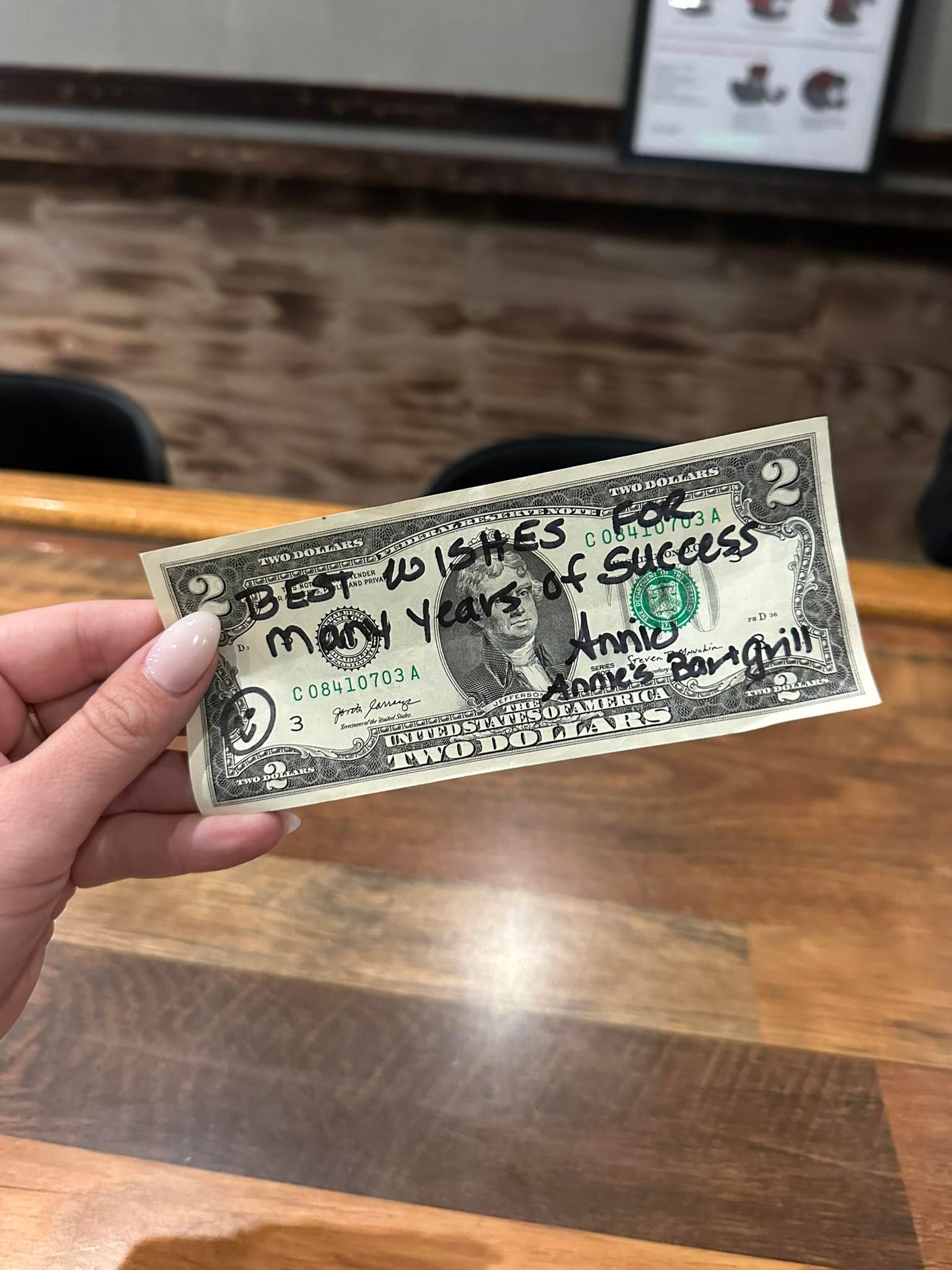 A person's hand holds a dollar bill with handwritten well wishes for 