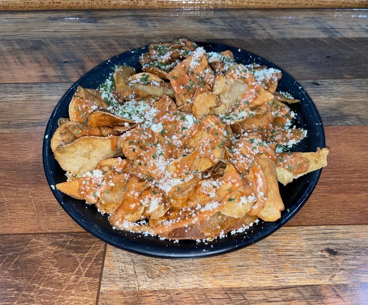 Plate of potato chips topped with orange sauce and white cheese, on a wood surface.