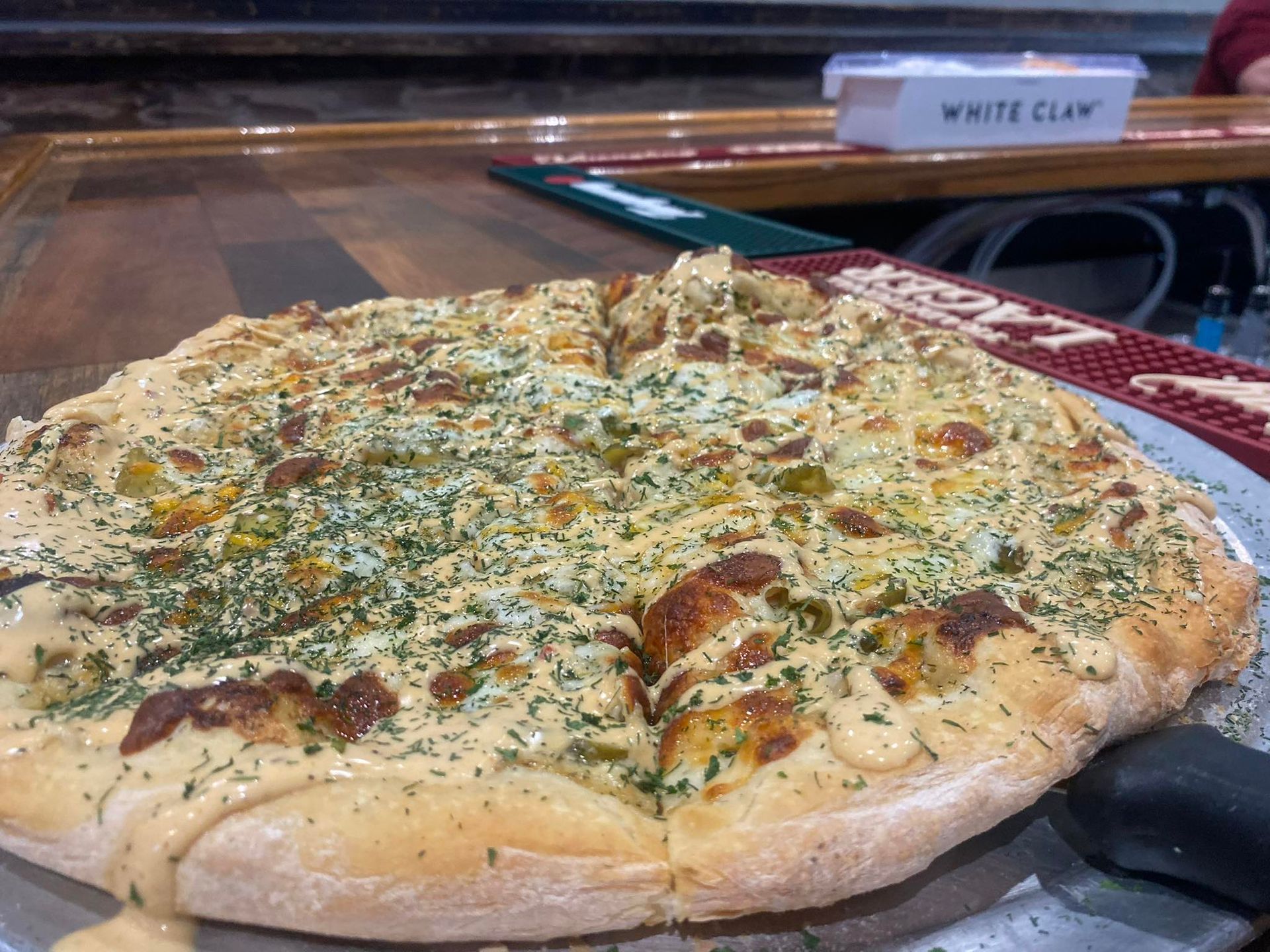 Pizza with creamy sauce, garnished with herbs, on a metal plate at a bar.