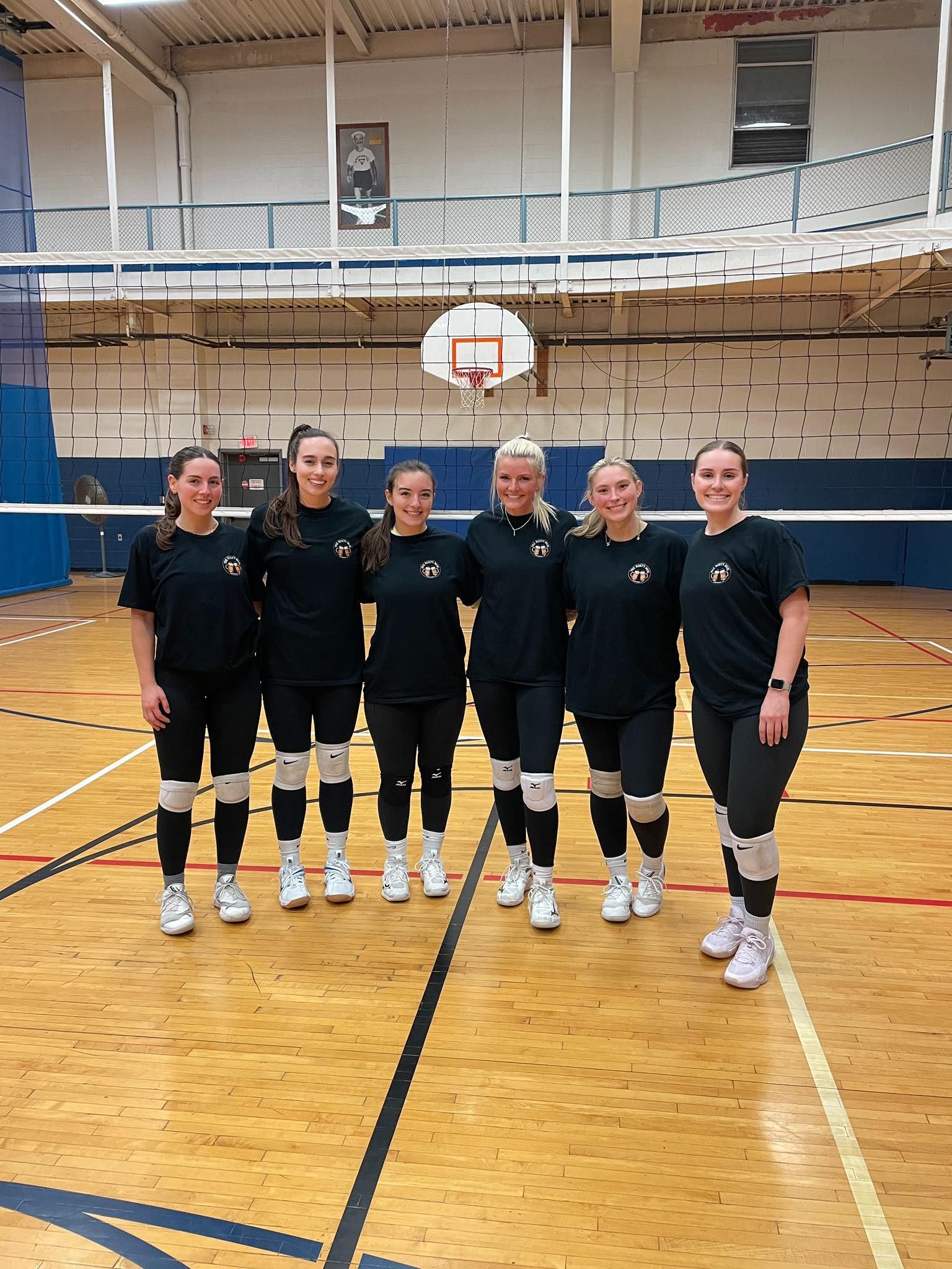 Six women in black volleyball uniforms pose on a court.