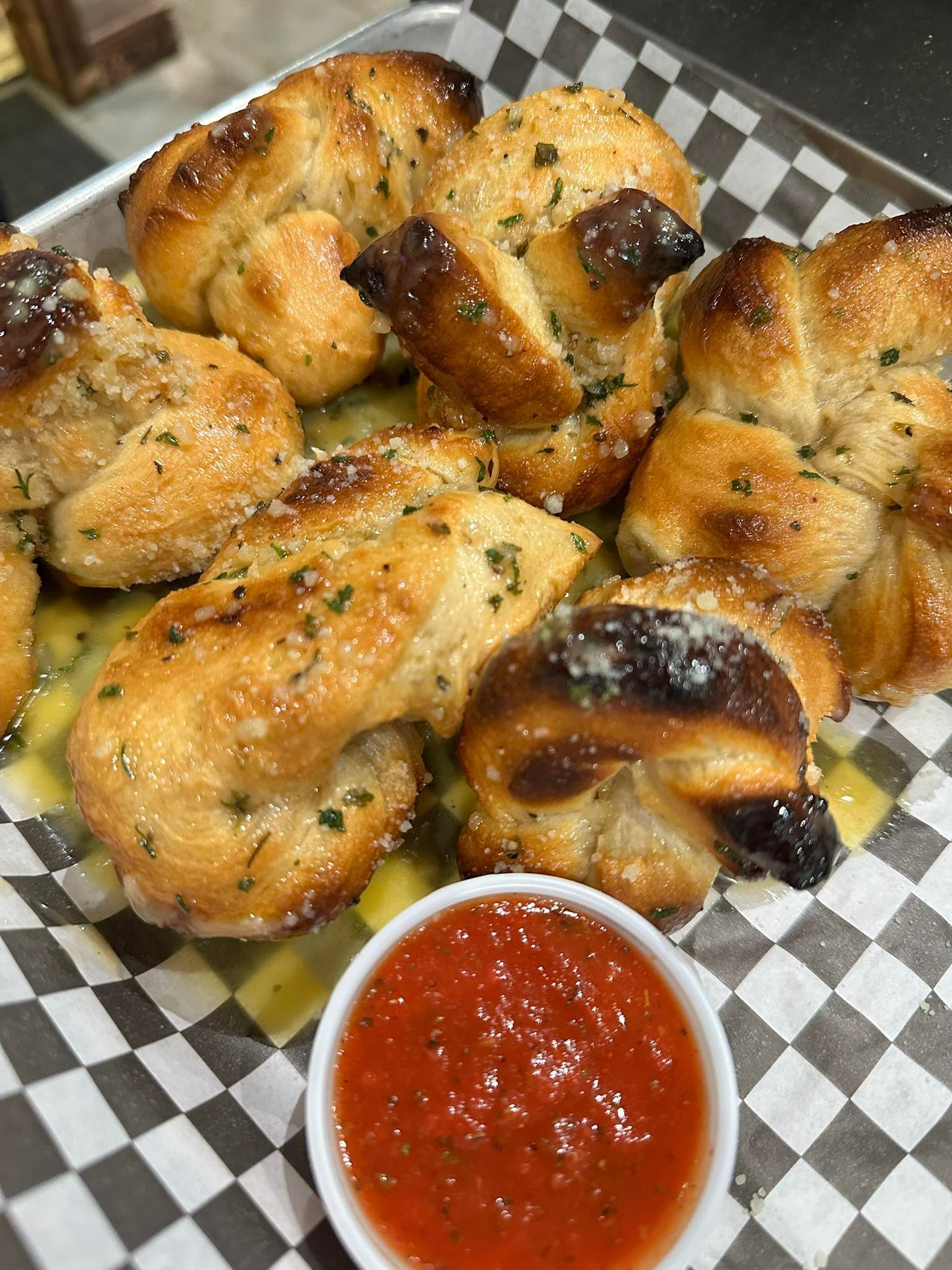 Garlic knots with sauce on checkered paper in a metal tray.