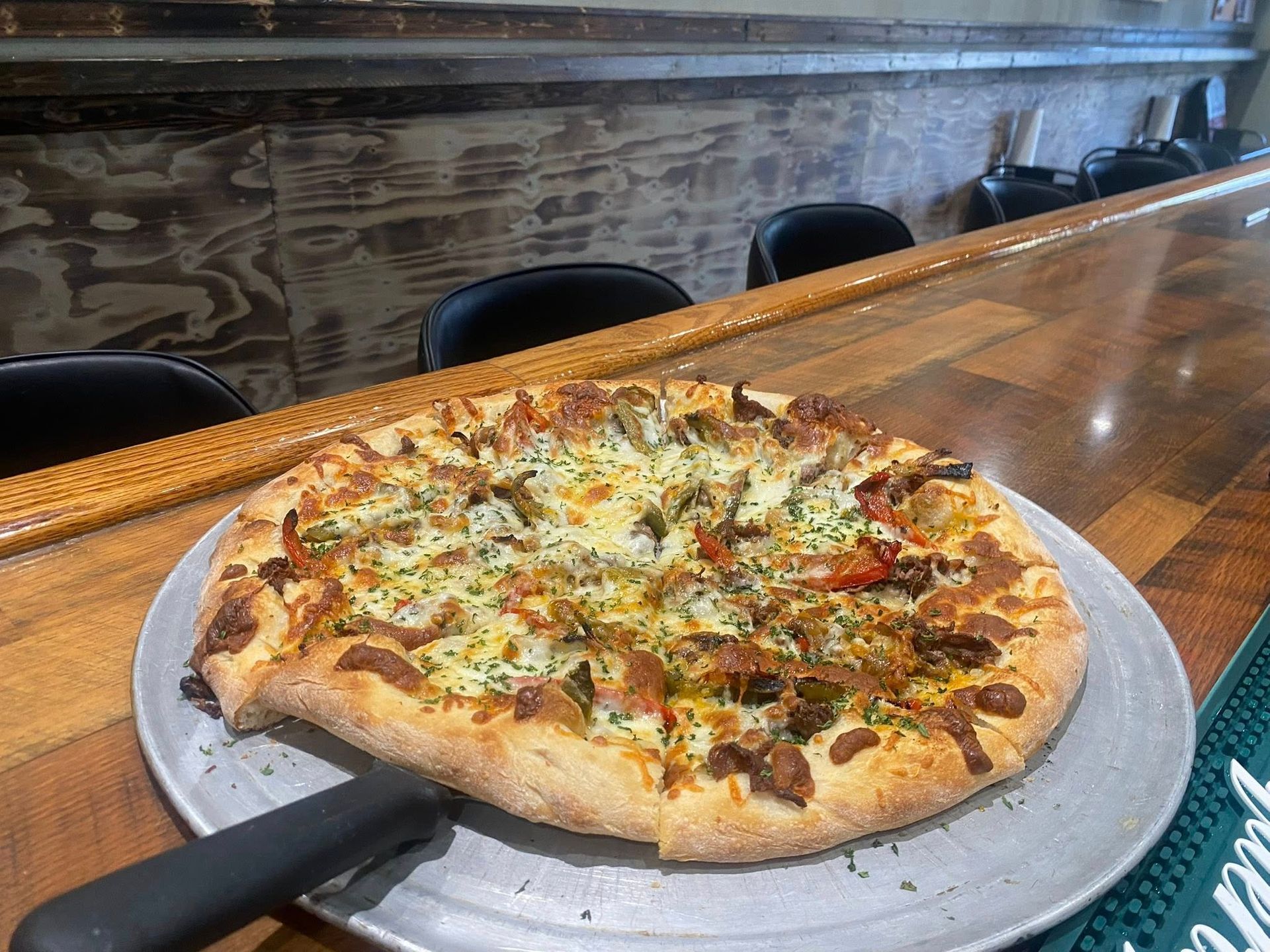 Pizza on a metal tray sits on a wooden bar.