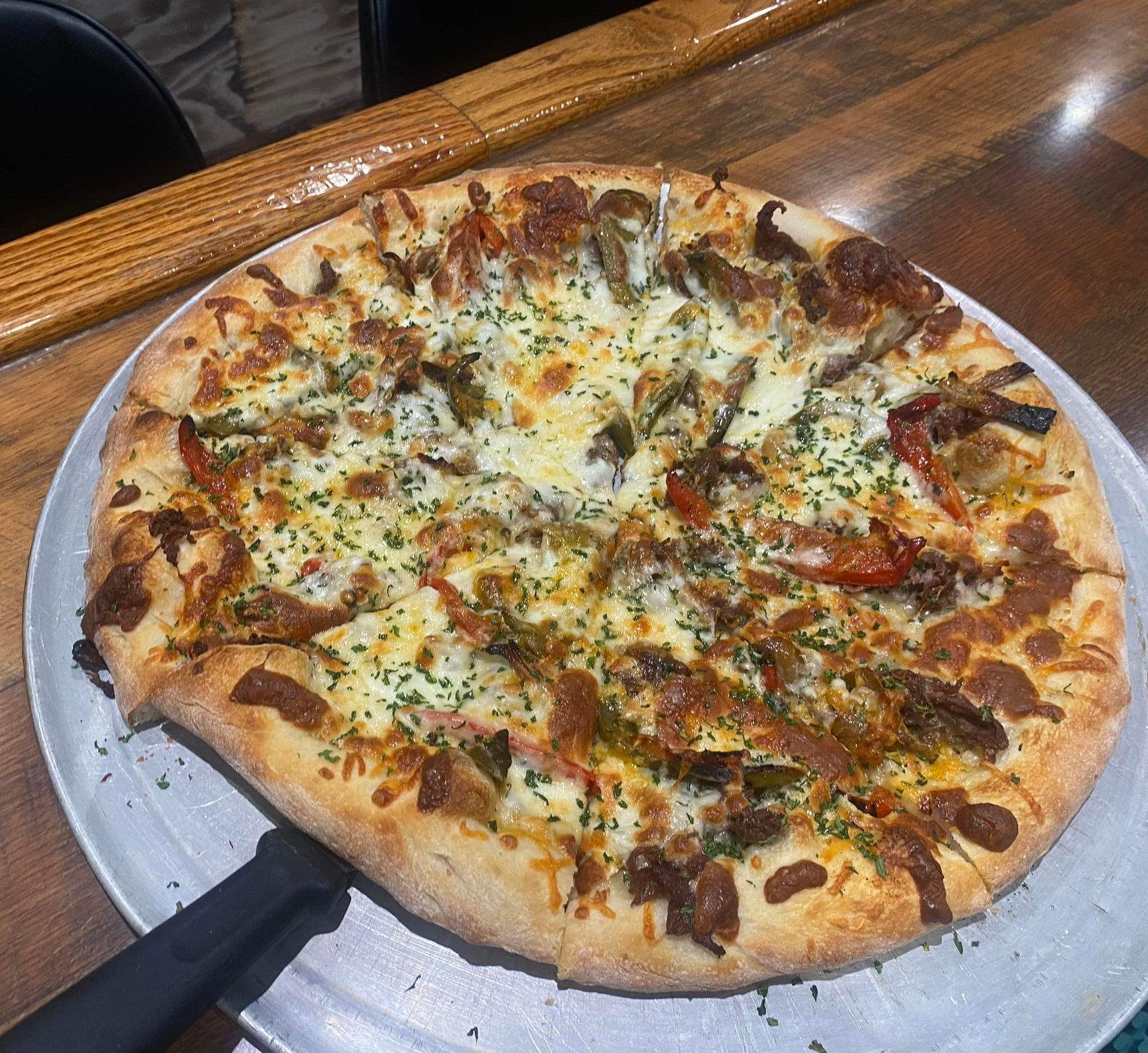 Pizza with toppings on a metal tray, on a wooden table.