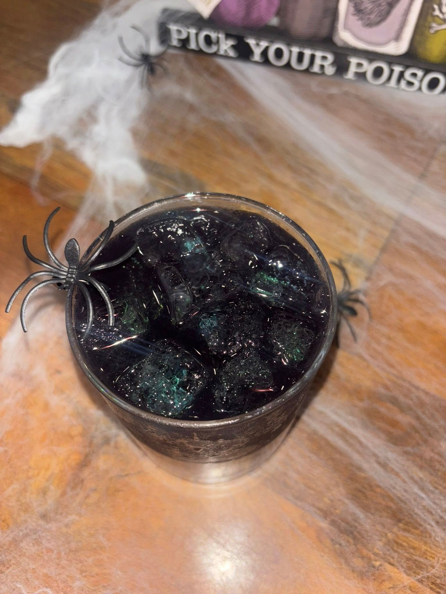 Halloween-themed drink with black liquid and glitter, fake spiders, and a 