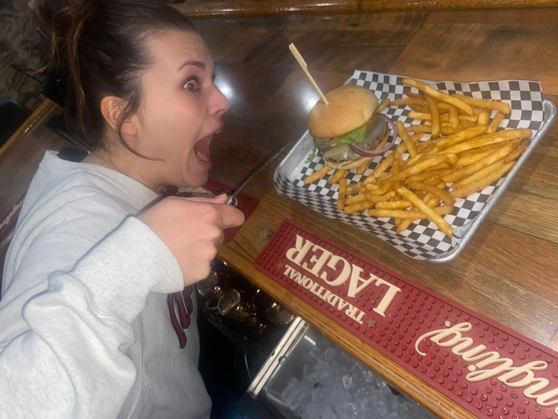 Woman with excited expression about to eat burger and fries on a tray.
