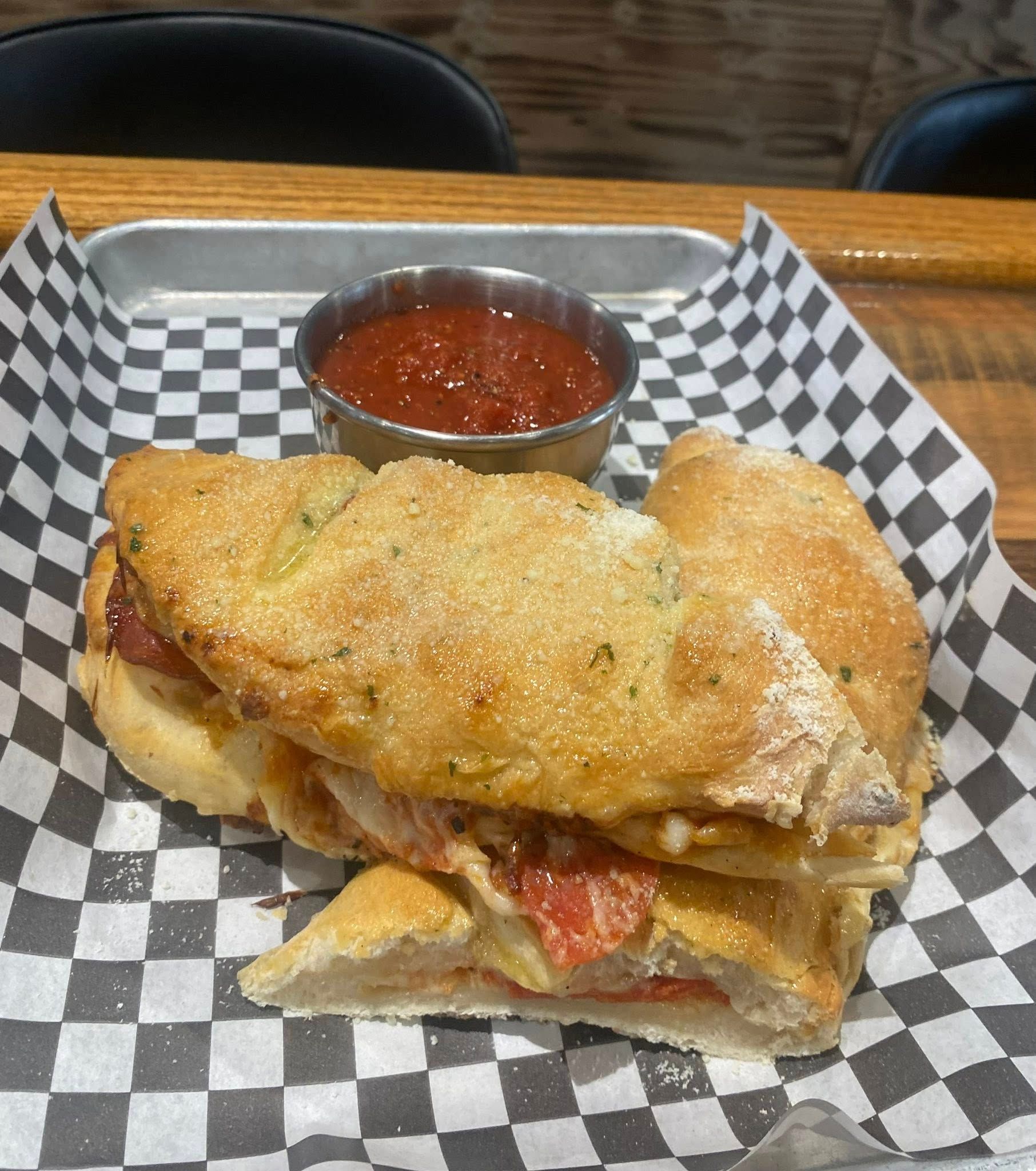Sandwich with tomato sauce in a small bowl, served on a checkered paper-lined tray.