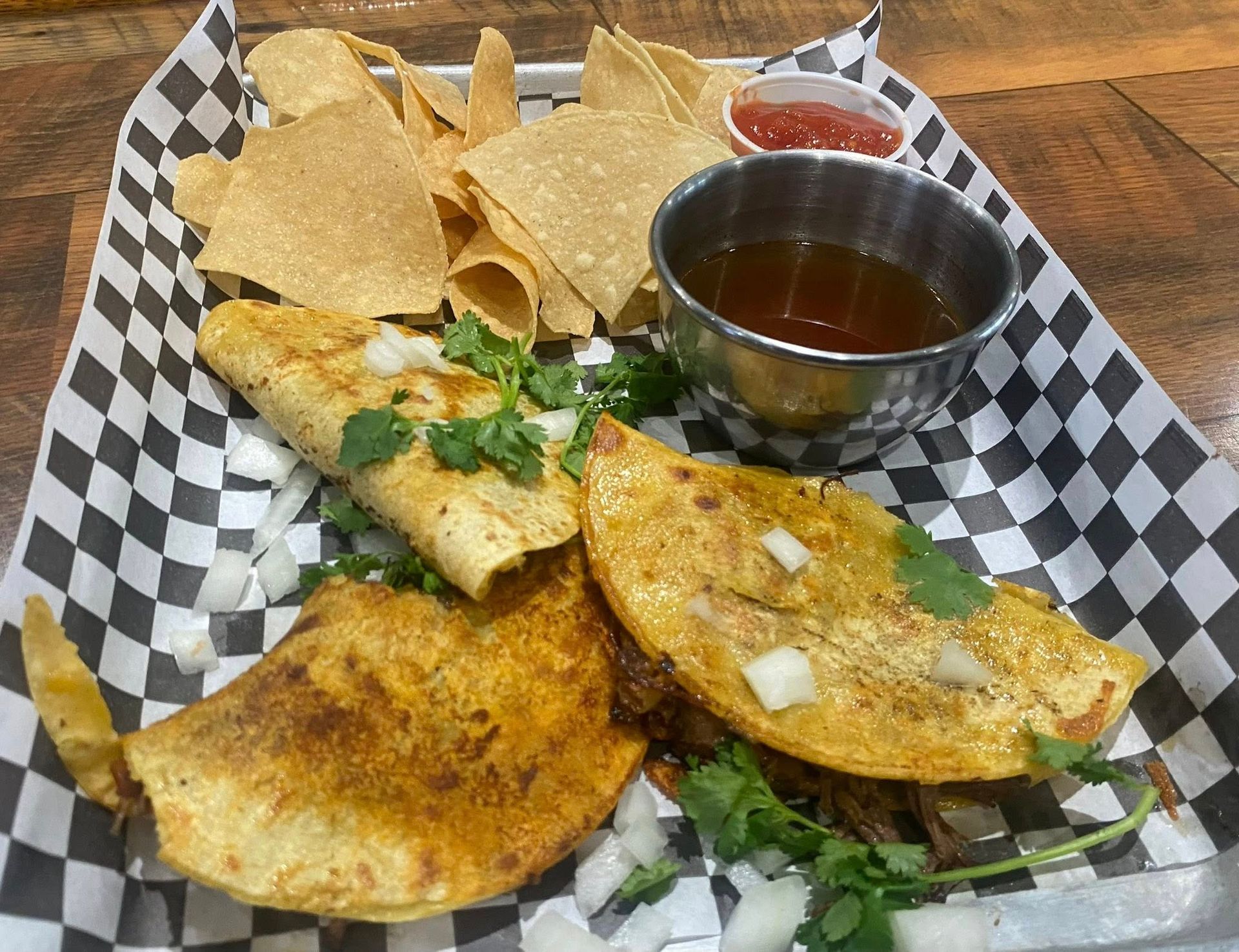 Birria tacos and chips on a tray with dipping sauces.