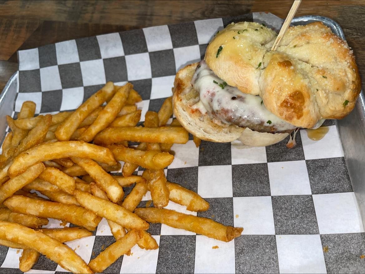 Burger with fries on a checkered paper-lined metal tray. The burger is held together with a toothpick.