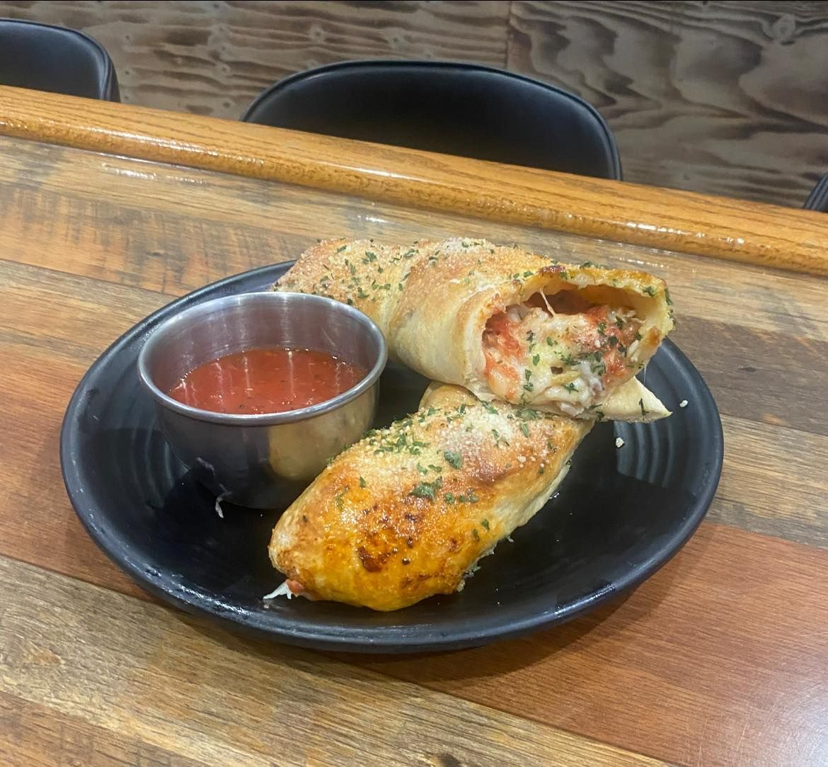 Pizza roll cut open on a plate with marinara sauce. It's on a wooden table.