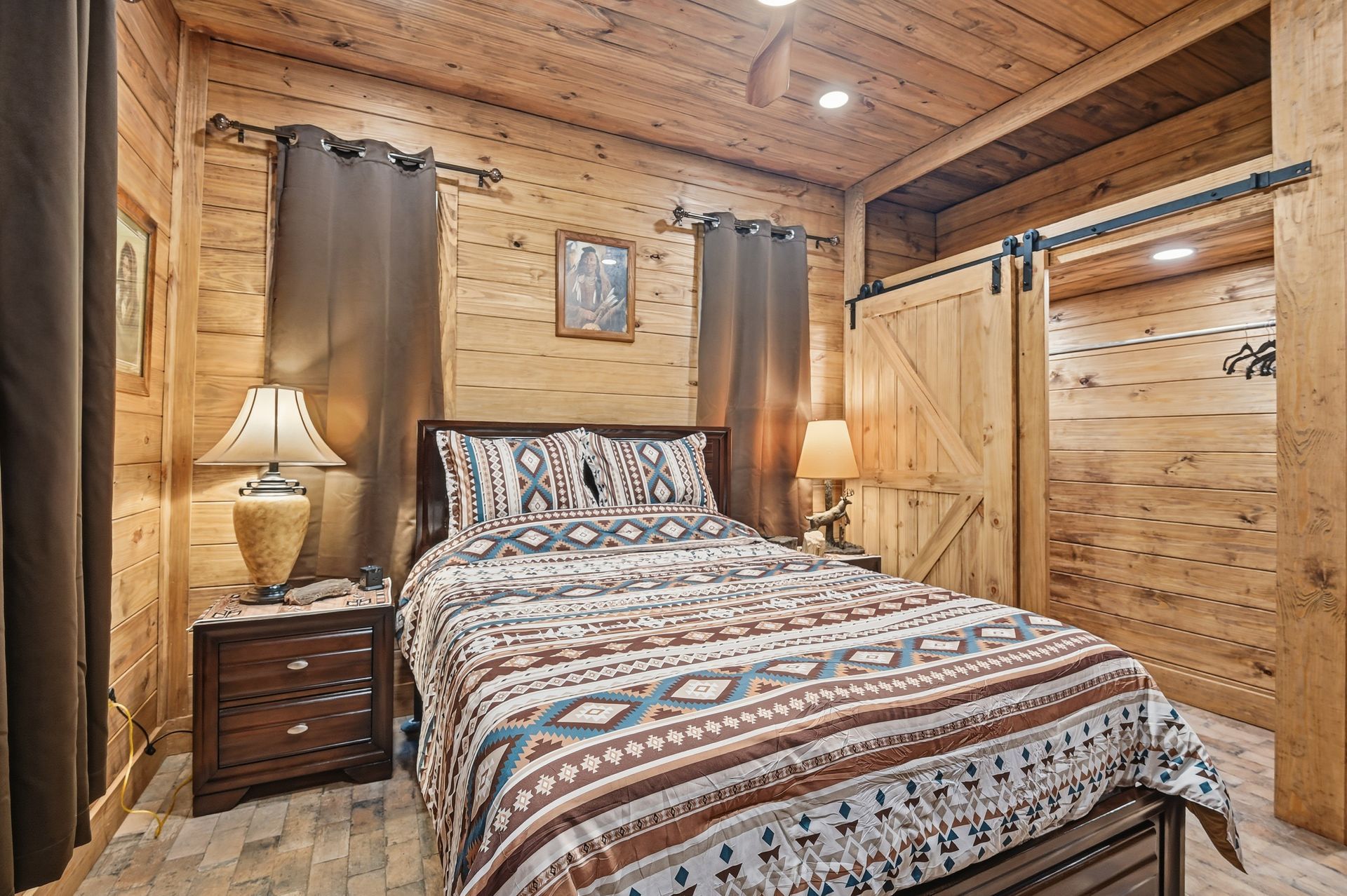 Rustic bedroom featuring a bed with patterned bedding, a dark wood nightstand, lamp, and sliding barn doors.