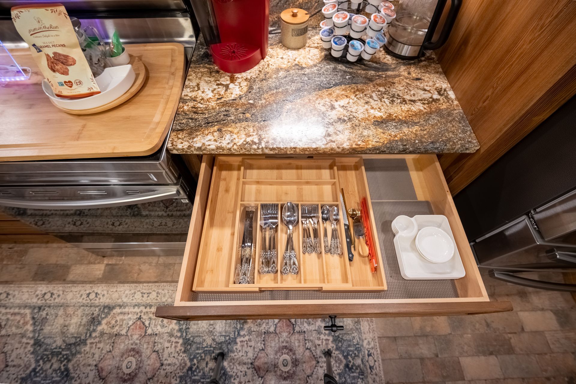 An open kitchen drawer containing a wooden cutlery organizer, next to a granite countertop with kitchen items.