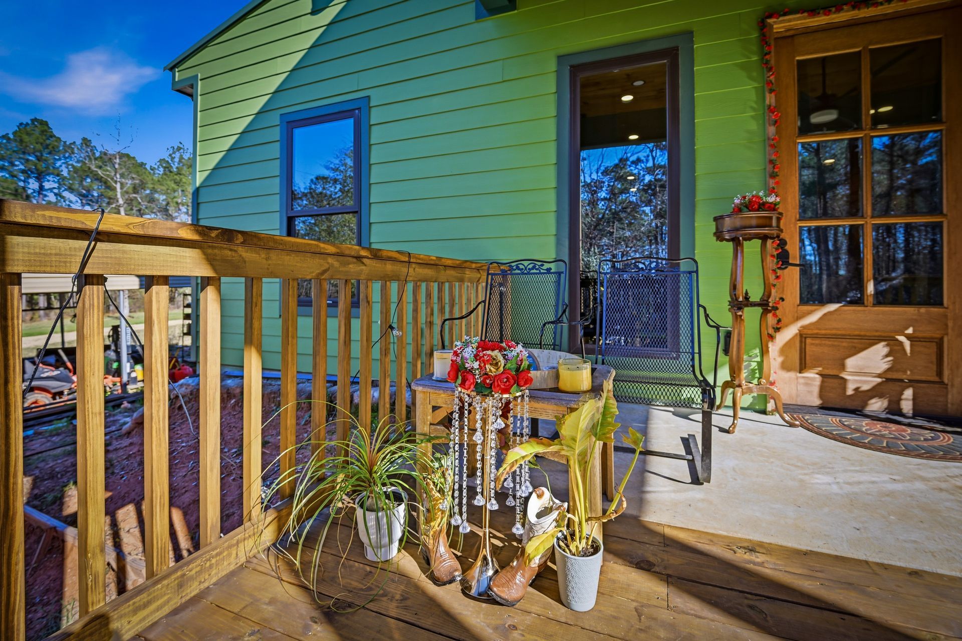 A green house with a wooden deck featuring a table, chairs, decorative hanging lights, and potted plants.