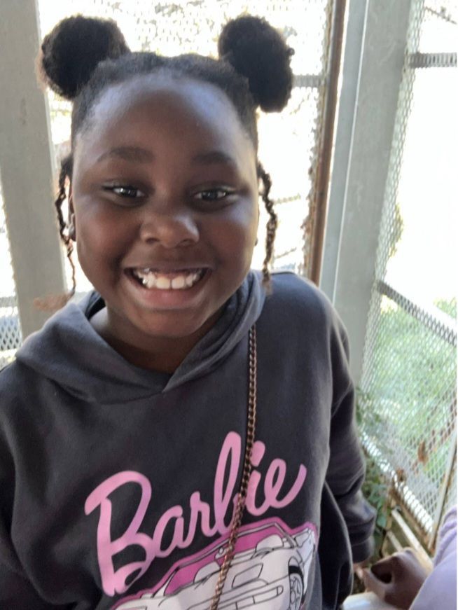 A girl wearing a barbie sweatshirt smiles for the camera