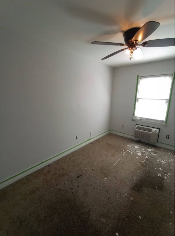 An empty room with a ceiling fan and a window.