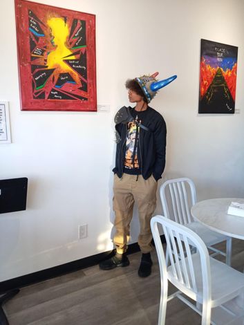A man wearing a party hat is standing in front of a painting