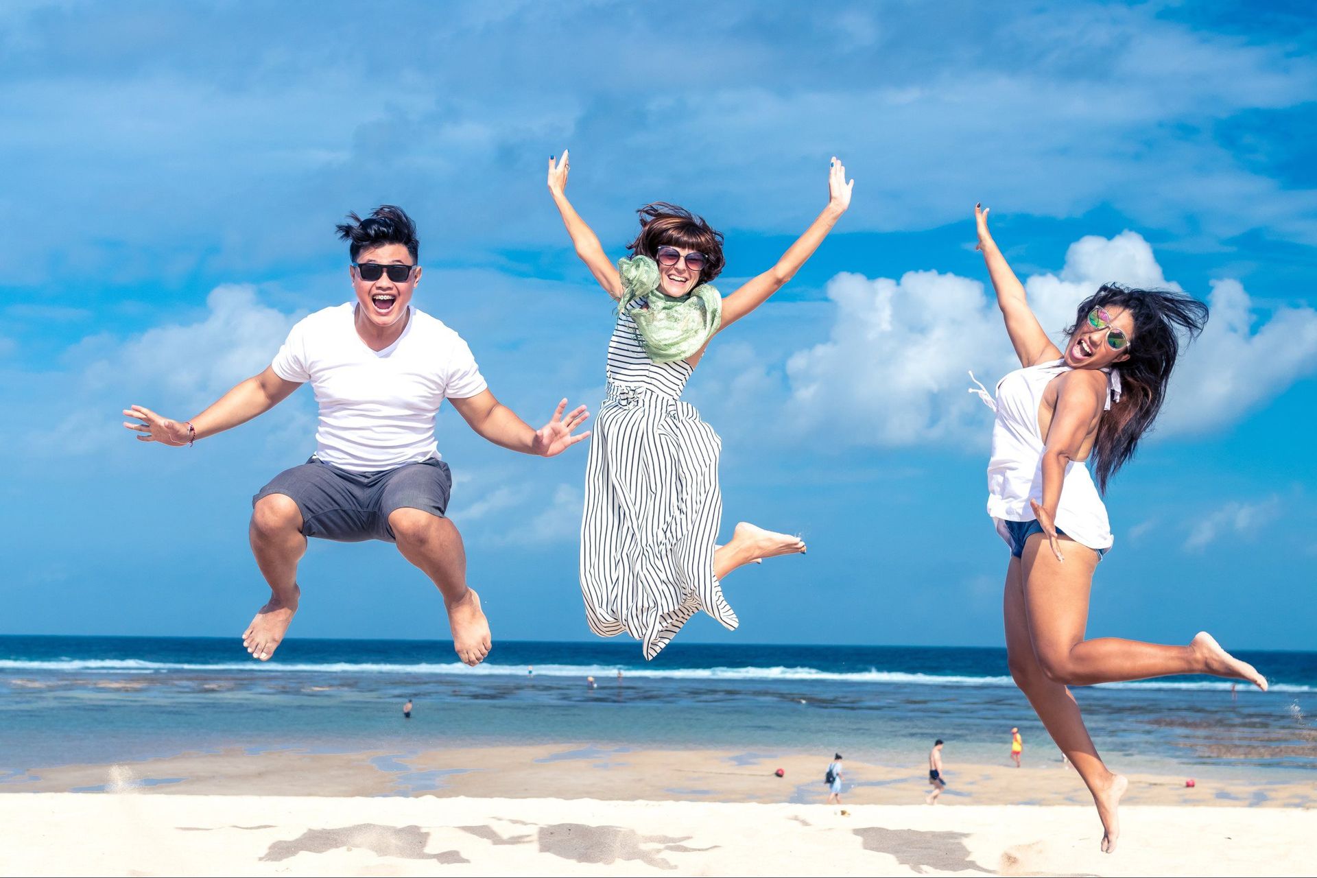 Three people jumping joyfully on a beach under a bright blue sky