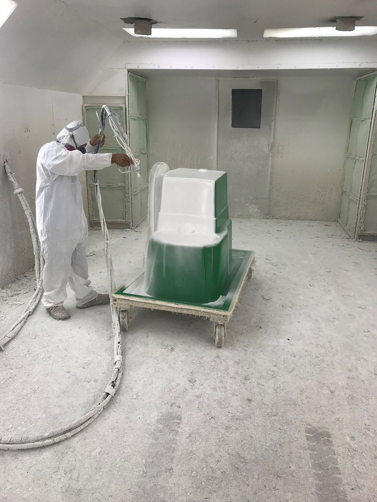 A man is spray painting a green object in a room.