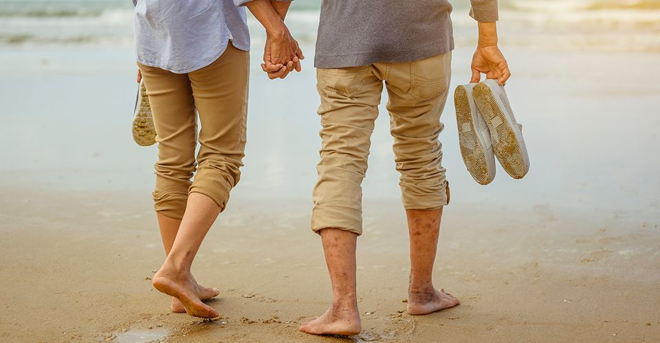 thumbnail of retired couple walking along a beach shoreline while carrying their shoes