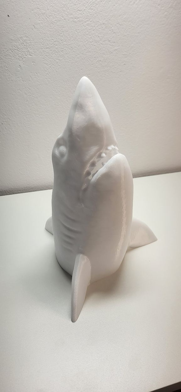 Een sculptuur van een witte haai op een witte ondergrond. De bek van de haai is open, waardoor de tanden zichtbaar zijn.