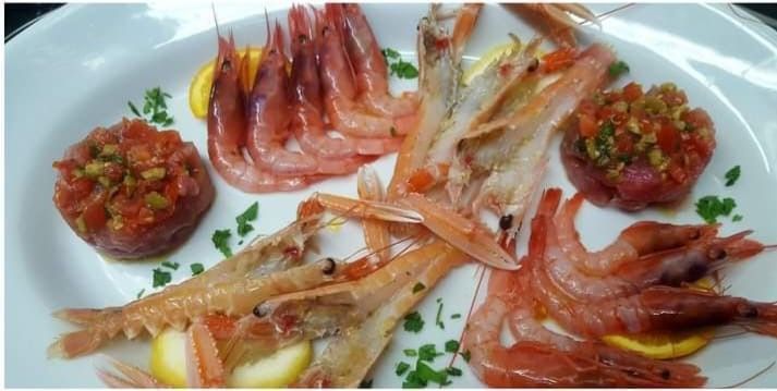 Un piatto bianco condito con gamberi e pomodori