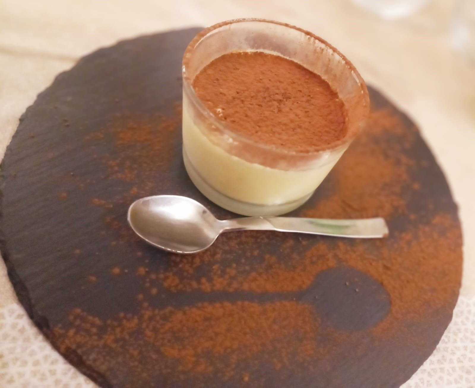 Una piccola tazza di dessert con un cucchiaio su un piatto