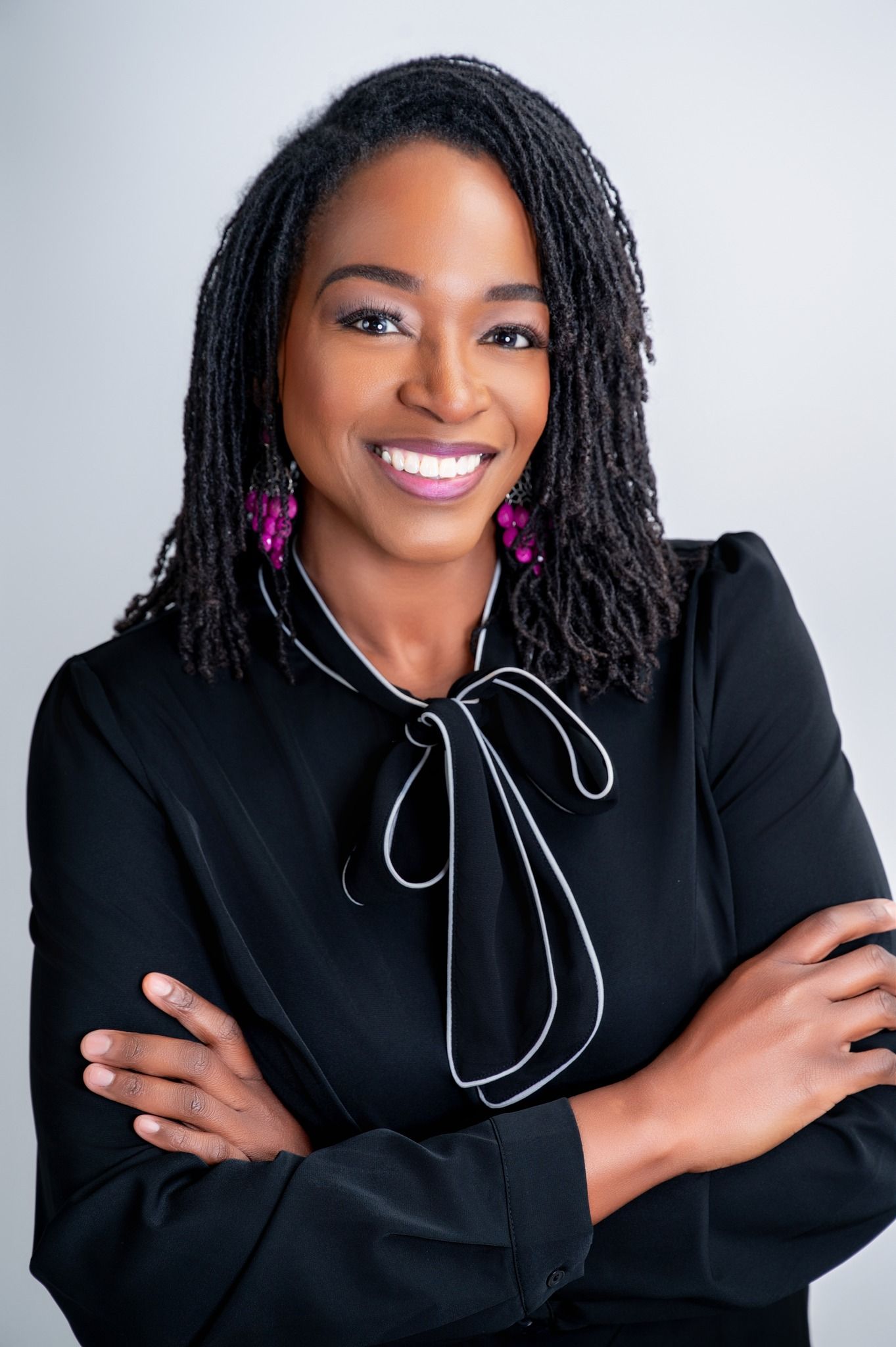 A woman wearing a black jacket and pearl necklace is smiling for the camera.