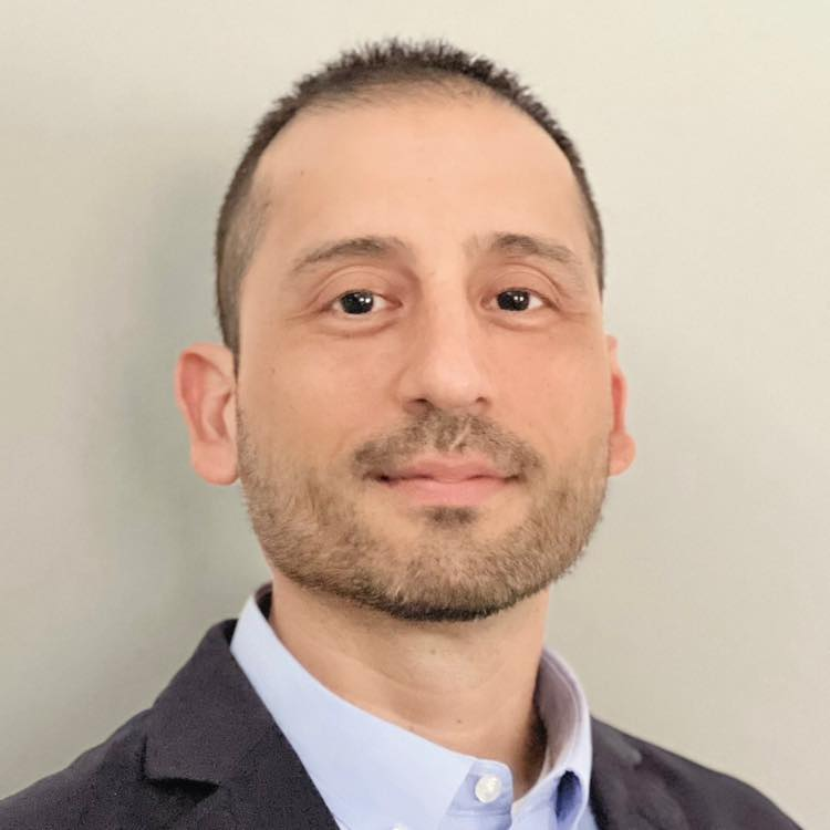 A woman wearing a black jacket and pearl necklace is smiling for the camera.