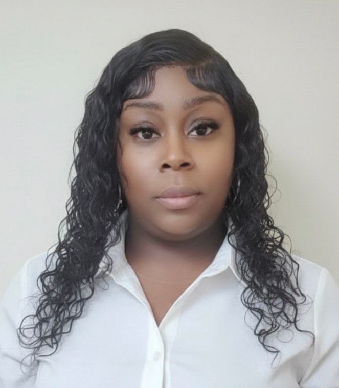 A woman wearing a black jacket and pearl necklace is smiling for the camera.