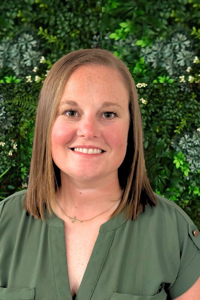 A woman in a green shirt is smiling in front of a green wall.