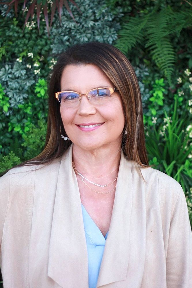 A woman wearing glasses and a tan jacket is smiling for the camera.