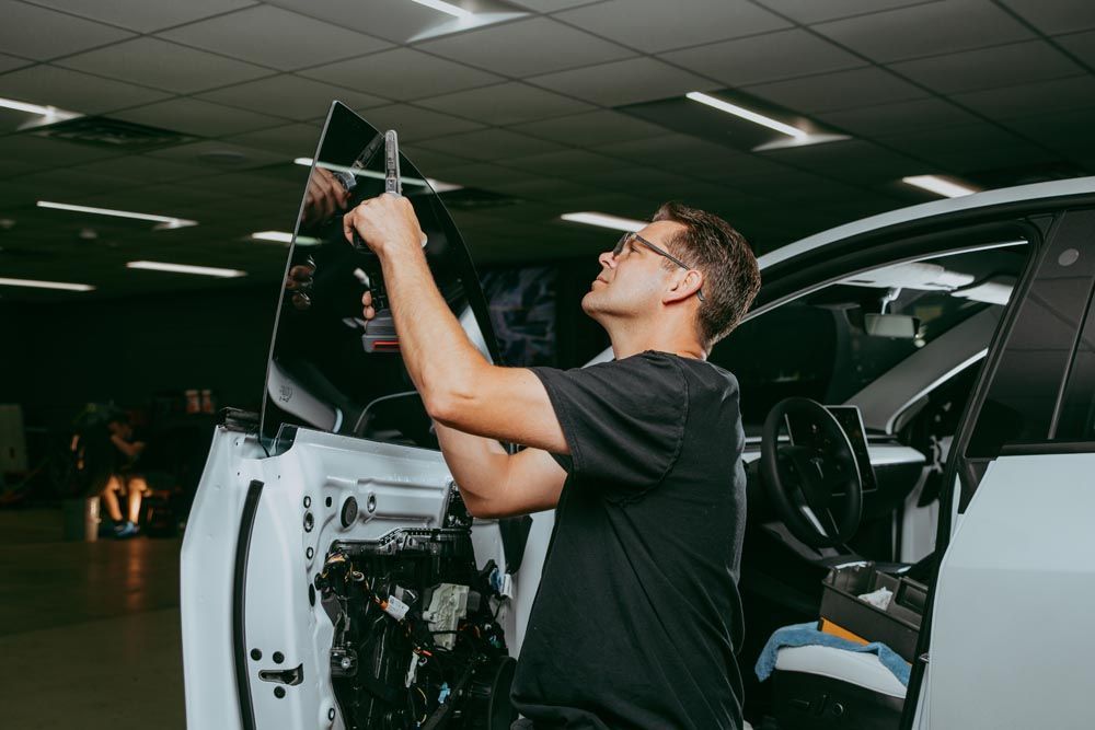 A person is installing window tint on a car. The person is inside the car looking up, wearing glasses.