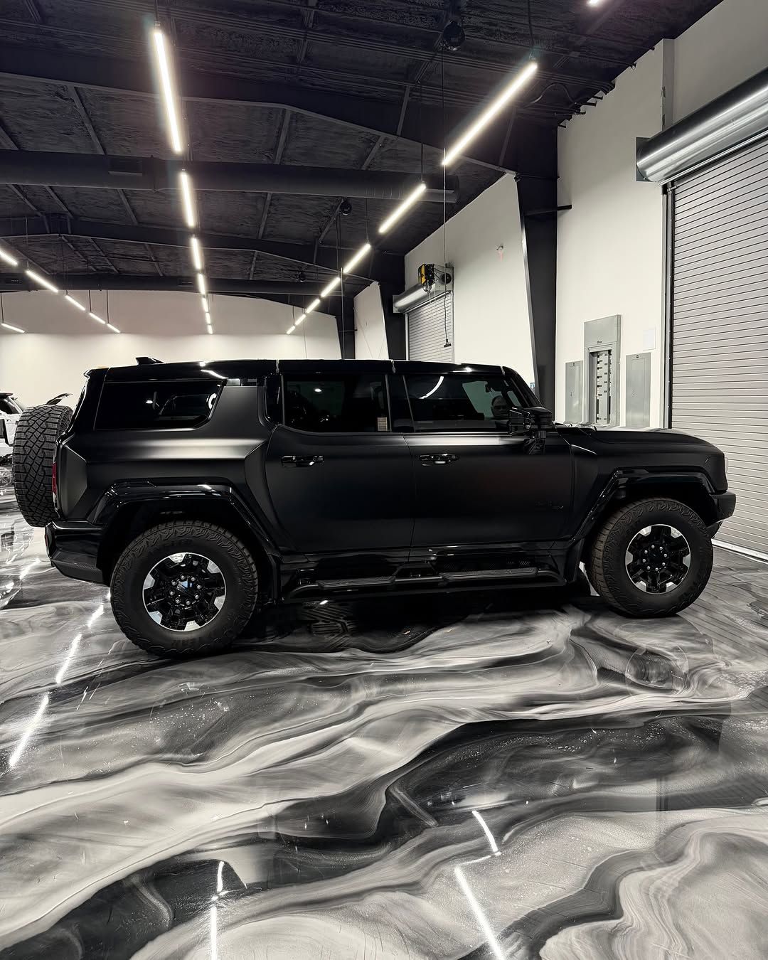 Black Hummer H3 SUV parked inside a garage with a decorative, grey epoxy floor.