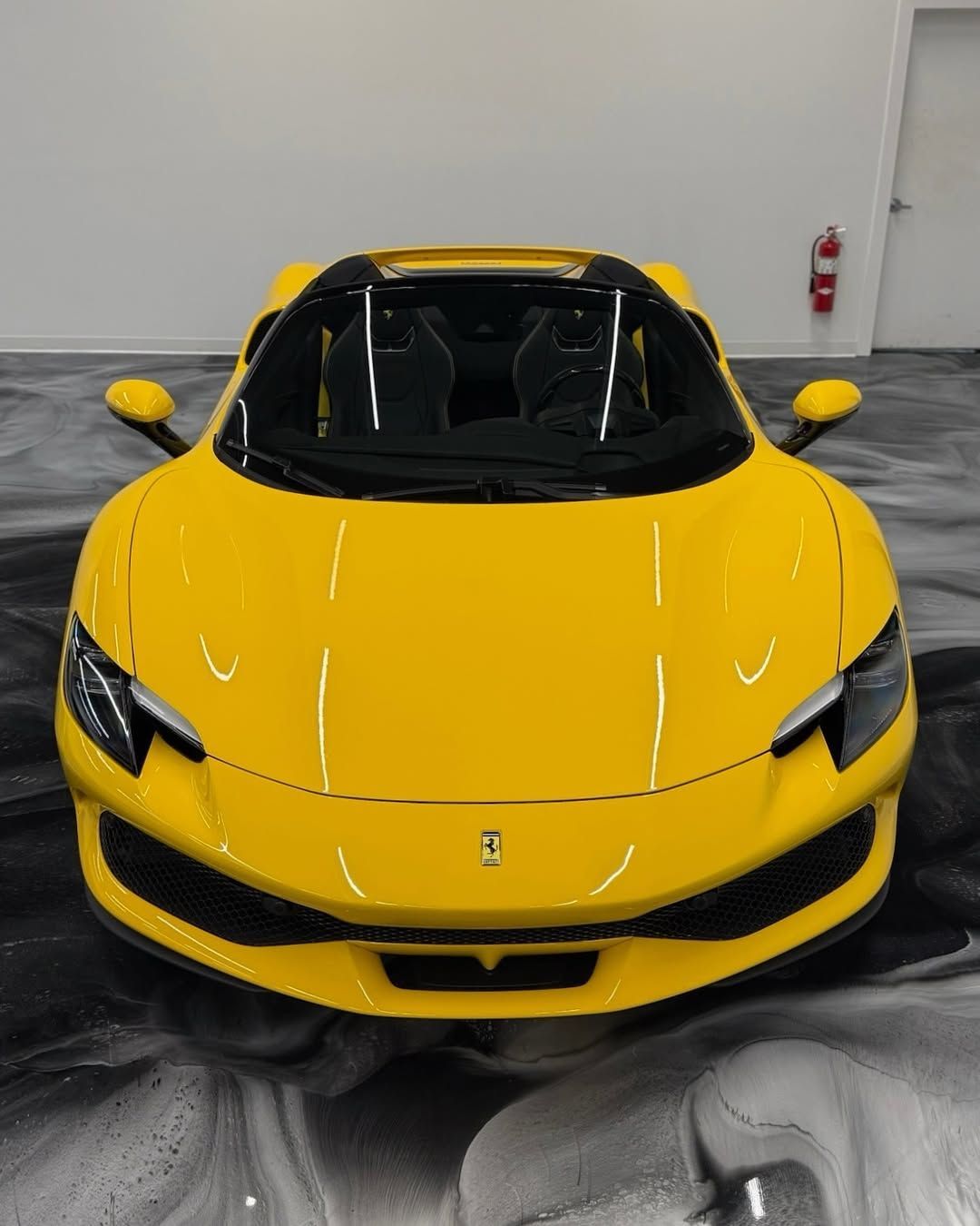 Yellow sports car in a garage with black and white flooring, viewed from the front.