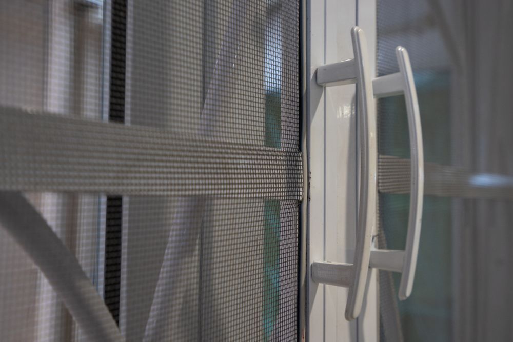 A White Sliding Screen Door Handle Attached to A Frame with A Grey Mesh Screen — LeSands Screens & Blinds Moss Vale Pty Ltd in Moss Vale, NSW