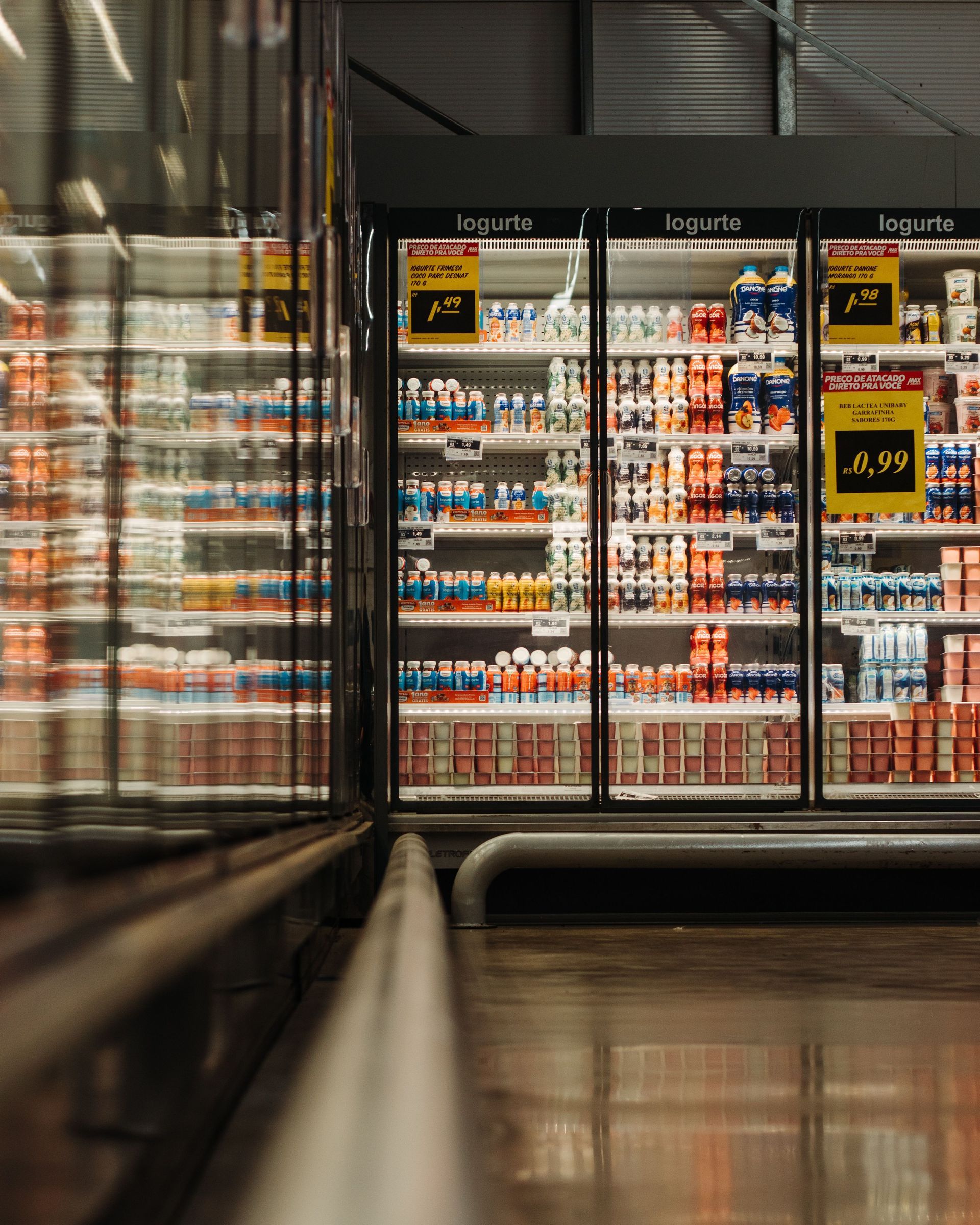 Supermarket freezer aisle with rows of colorful drinks behind glass doors