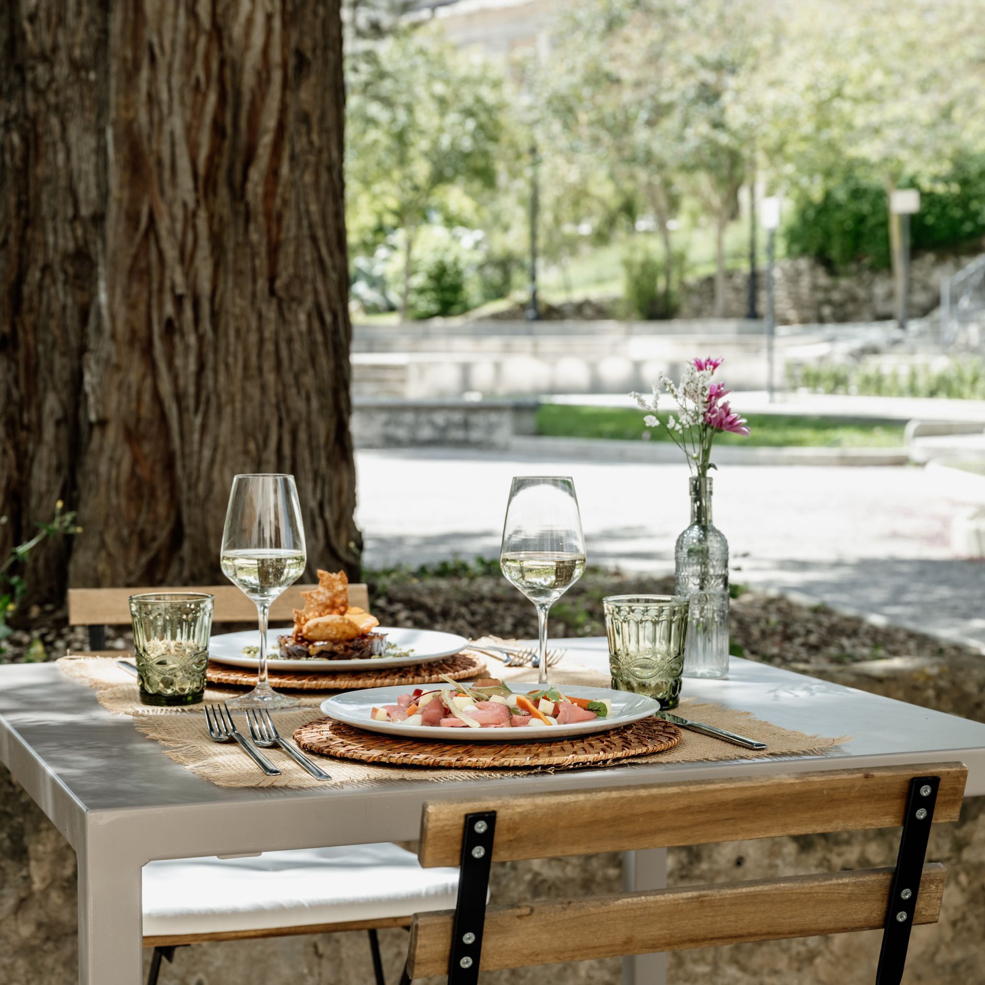 Un tavolo con sopra piatti di cibo e bicchieri di vino in un vigneto. Prenota l'aperitivo in vigna all'Antico Convento.