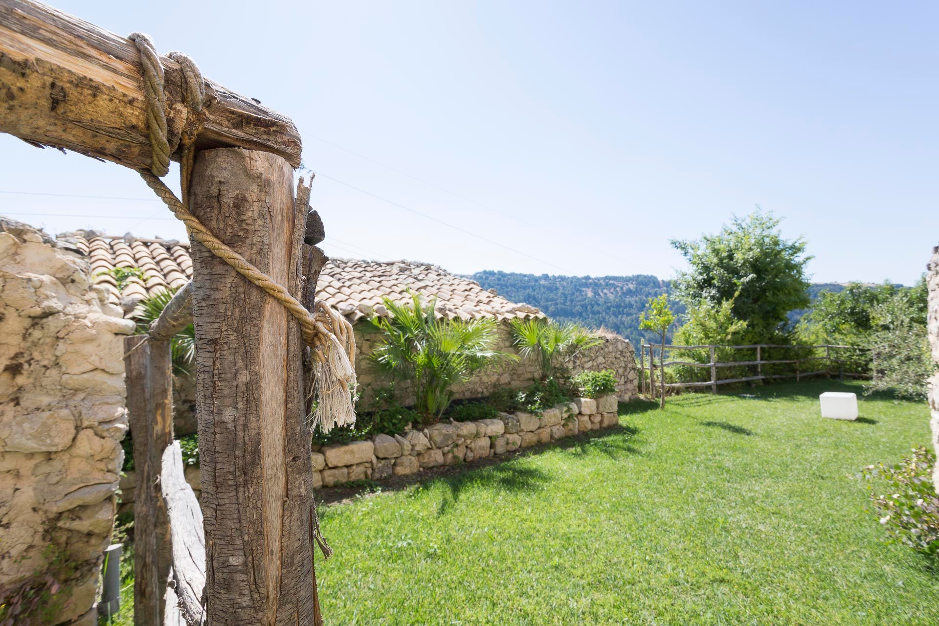 Un palo di legno a cui è attaccata una corda è circondato dall'erba e da un muro di pietra | Antico Convento dei Cappuccini