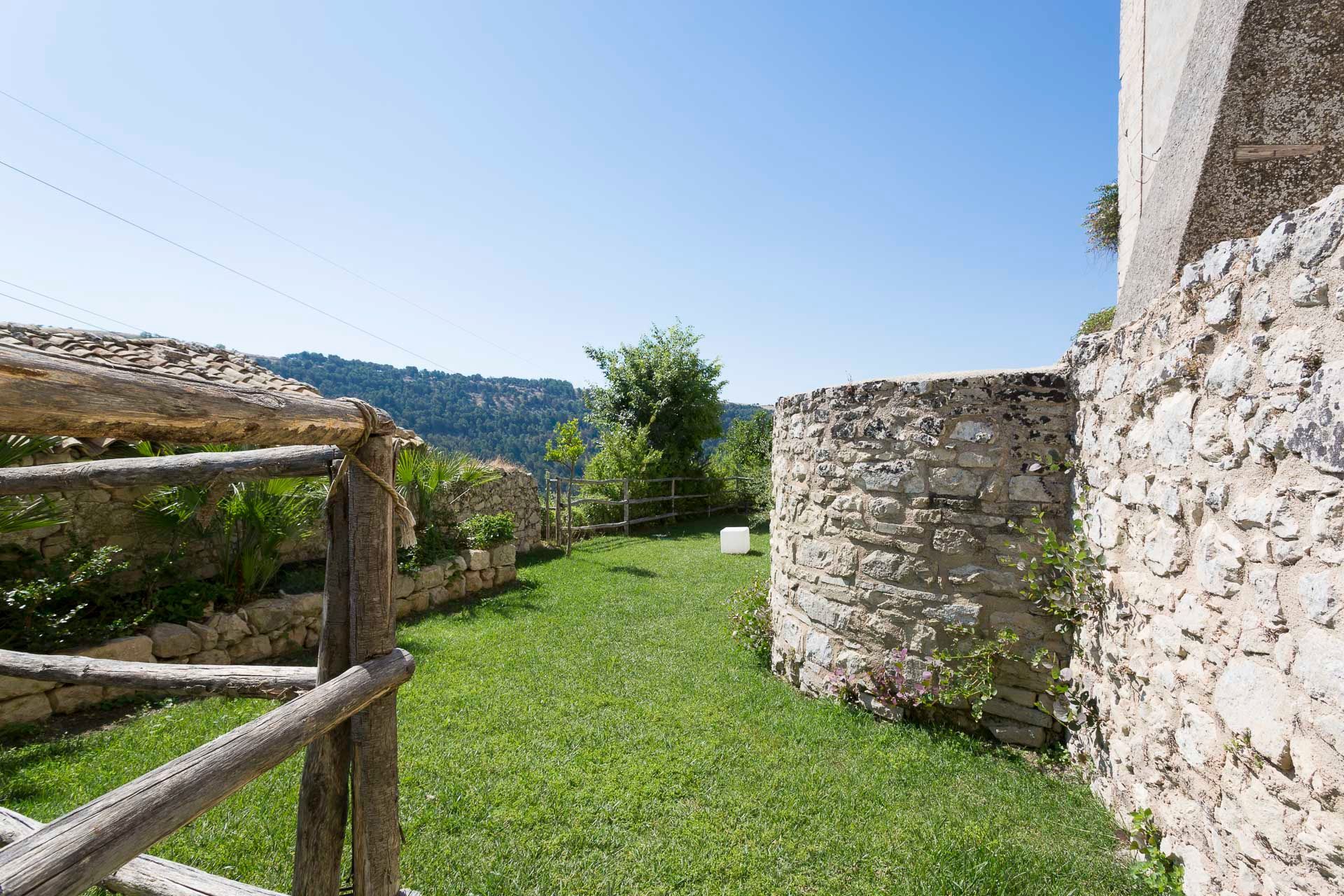 Una staccionata in legno circonda un rigoglioso prato verde accanto ad un muro di pietra  | Antico Convento dei Cappuccini