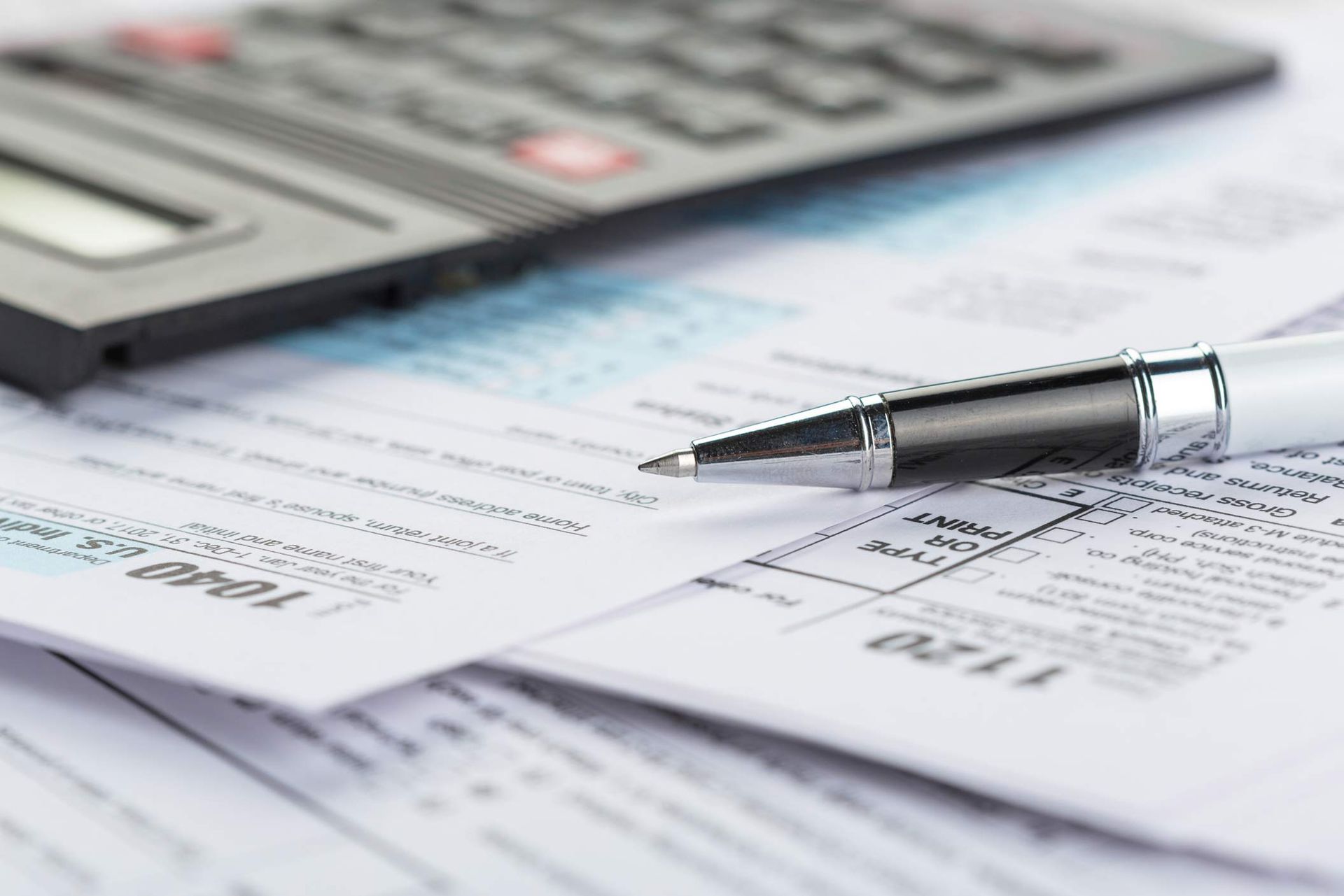 A pen is sitting on top of a pile of papers next to a calculator.