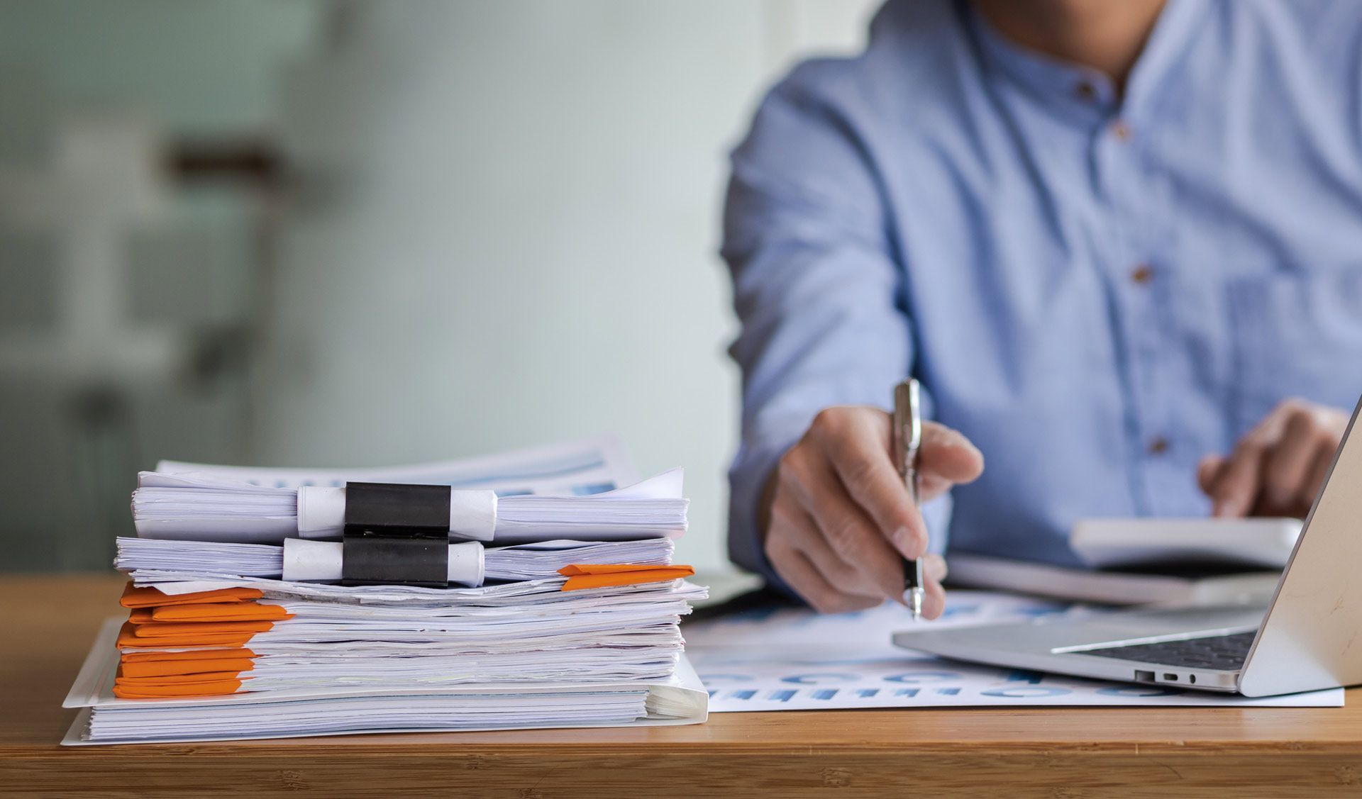 A man is sitting at a desk with a stack of papers and a laptop.