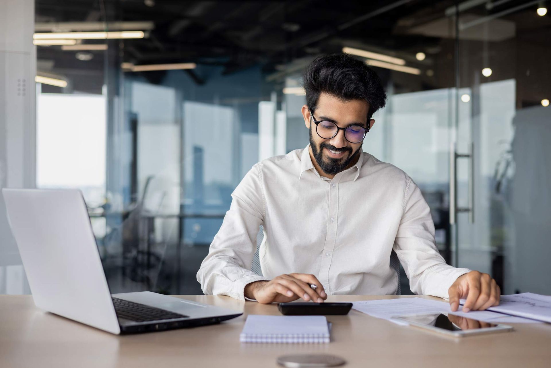A man is sitting at a desk with a laptop and a calculator.
