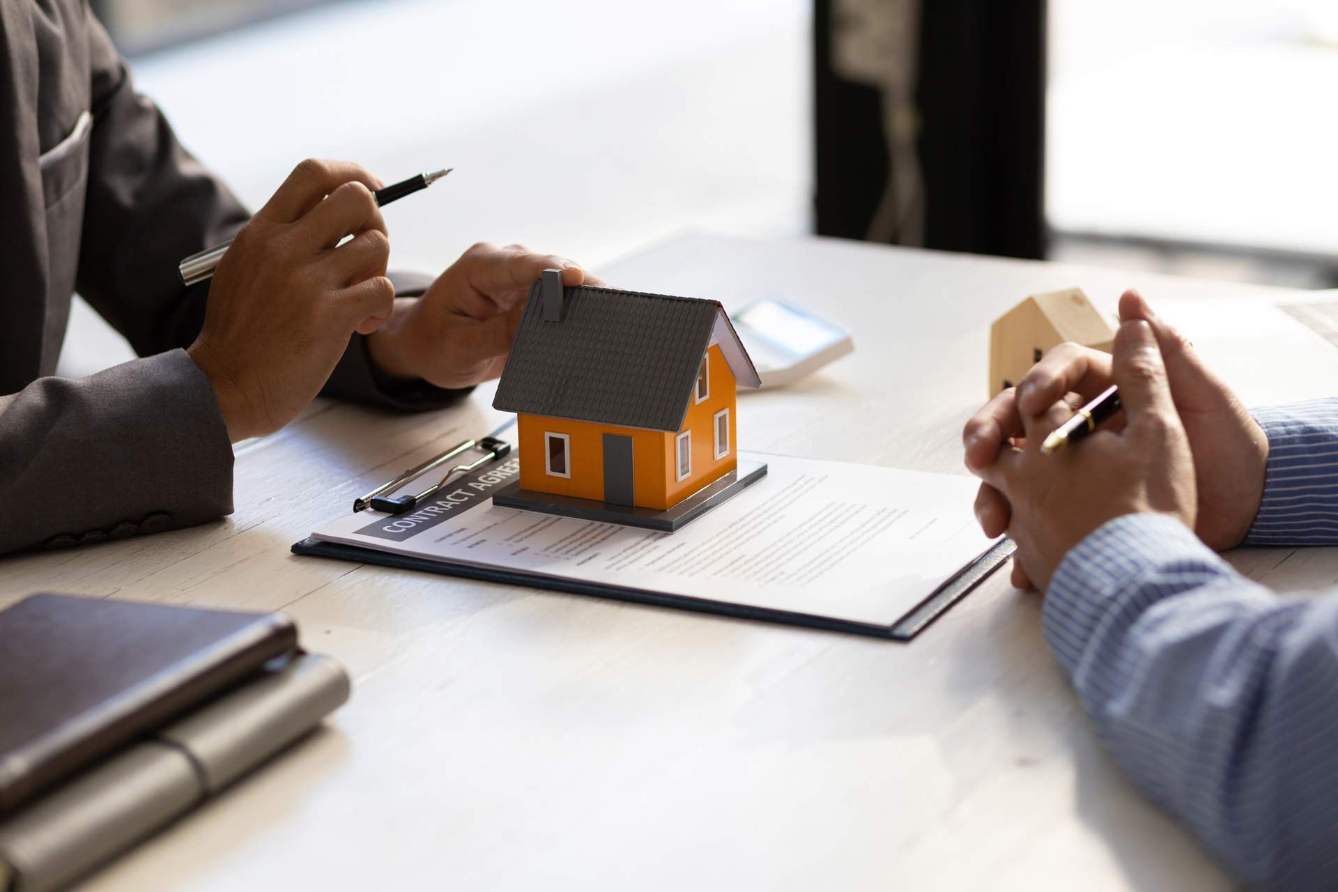 A man is sitting at a table with a model house on top of a clipboard.