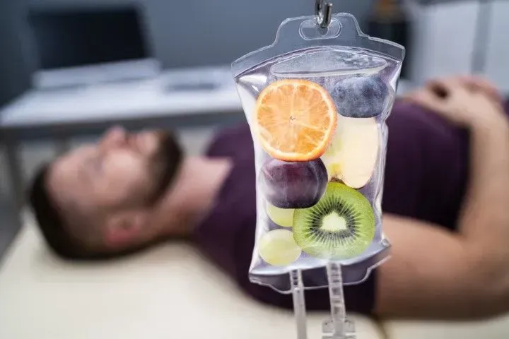 Close-up of an IV bag filled with fresh fruit slices over a resting patient.