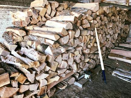 Pile of cut firewood stacked in a shed with a long-handled tool leaning against it.