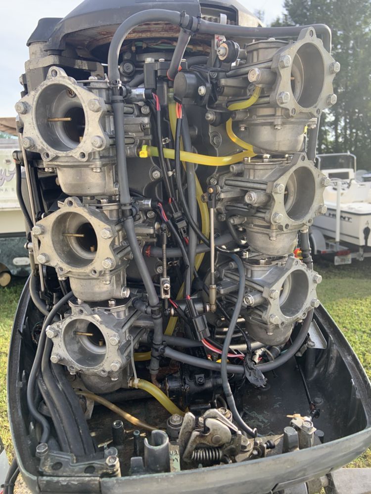 Close-up of a disassembled outboard motor with six carburetors visible, showing internal engine components and yellow fuel lines.